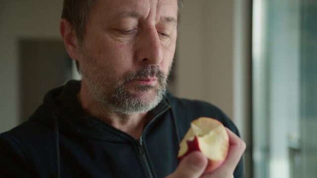 Closeup of mature man eating red apple by the apartment window in morning, 4K
