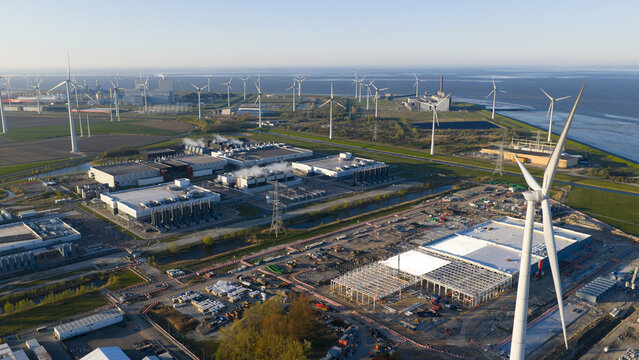 Aerial view of the industrial port area featuring numerous wind turbines, large data centers, and construction sites under a clear sky in Eemshaven, Groningen, Netherlands.