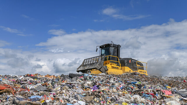 Heavy industrial machinery working at a large landfill site.  A view on a landfill compactor compacting and managing piles of waste.