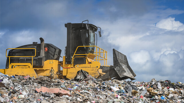 Heavy industrial machinery working at a large landfill site.  A view on a landfill compactor compacting and managing piles of waste.