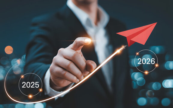 Man's hand launching red paper airplane with growth arrow from 2025 to 2026 over bokeh city lights