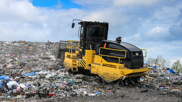 Heavy industrial machinery working at a large landfill site.  A view on a landfill compactor compacting and managing piles of waste.