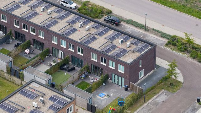 Aerial view of modern terraced houses in the Nobelhorst neighborhood featuring solar panels on flat roofs and private backyards in Almere, Flevoland, Netherlands.