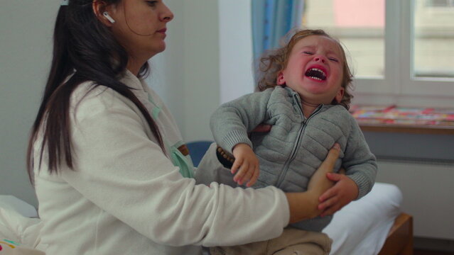 Mother comforting distressed toddler in arms, steady embrace patience and emotional containment during challenging caregiving moment at home