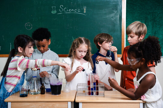 Diverse elementary students performing science experiment in classroom laboratory, exploring chemistry and teamwork. STEM education, curiosity, learning, innovation and child development concept.