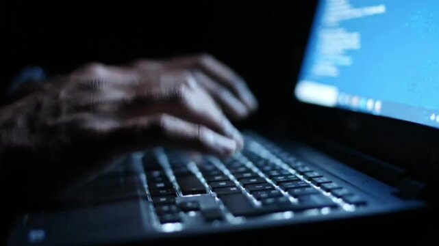 Close up of human hands typing on illuminated keyboard of modern laptop in dark room at night focusing on fast motion and software development coding activity.