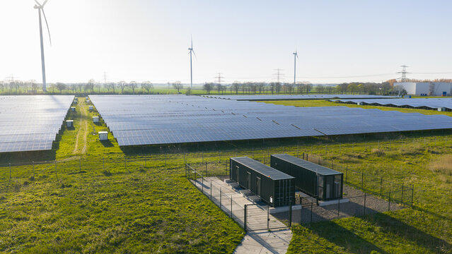 Aerial view of Solar park Delfzijl featuring rows of photovoltaic panels and wind turbines under a clear sky in Farmsum, Groningen, Netherlands.