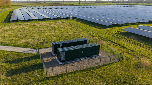 Aerial view of Solar park Delfzijl featuring rows of photovoltaic panels and green industrial containers on a grassy field in Farmsum, Groningen, Netherlands.