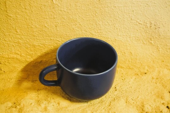 Blaue Kaffeetasse steht auf rauer gelber Betonfl&auml;che vor gelber Wand 