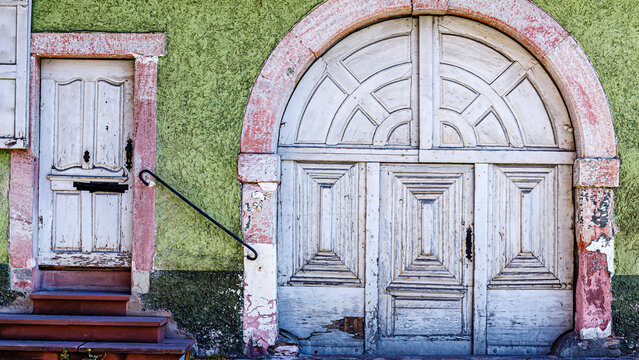 Old wooden doors and a small side door on a green wall in a quiet neighborhood during daytime