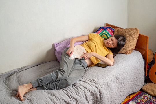 Young woman with a colostomy bag lies on her bed at home