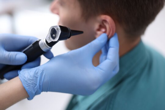Hearing test. Doctor examining man's ear with otoscope in clinic, closeup