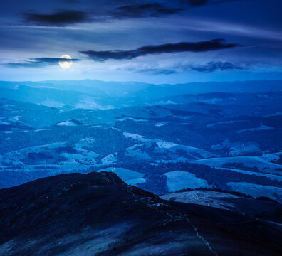 mountainous countryside scenery at night. view of cloudy sky above the valley. full moon over colorful meadows and trees on hill in dappled light. mysterious nature scenery of carpathians