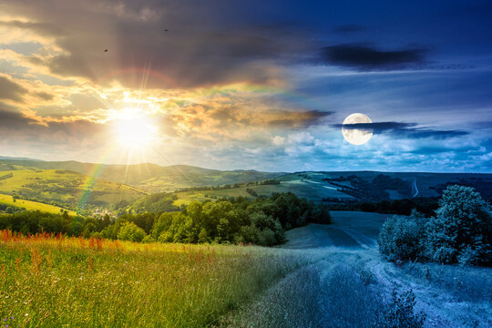 day meet night in beautiful countryside. epic view landscape in mountains on summer solstice. sun and moon in harmony over trail through the grassy field near forested rolling hills. rural scenery