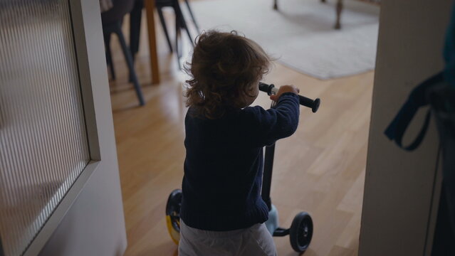 Toddler removing helmet then pushing scooter forward before stumbling and pausing on floor showing gentle vulnerability determination and early exploration inside warm family home