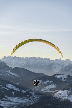Paragliding in the air in front of snow-covered Alps in winter, Brixen im Thale, Tyrol, Austria
