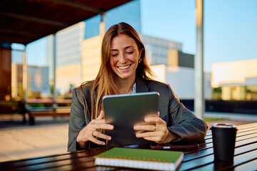 Professional young businesswoman smiling while working with a digital tablet on an outdoor terrace,...