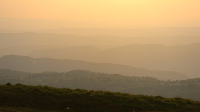 Aerial view of the rolling mountain ridges of Le Colomby de Gex during a hazy golden hour sunset in Echenevex, Auvergne-Rhone-Alpes, France.