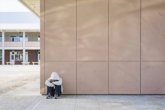 Enfant seul assis au sol dans une cour d&rsquo;&eacute;cole exprimant tristesse, isolement et harc&egrave;lement scolaire