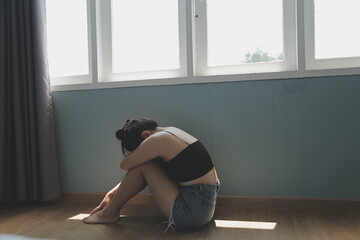 Fototapeta premium Woman sitting on floor in thoughtful pose near large window with natural light streaming in