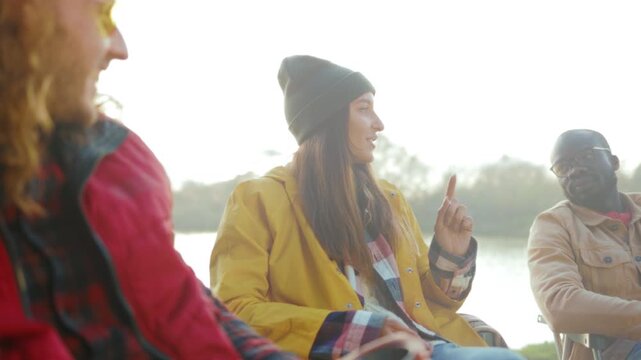 Woman laughs outdoors, Smiling woman wearing bright jacket and beanie chatting freely beside peaceful lake
