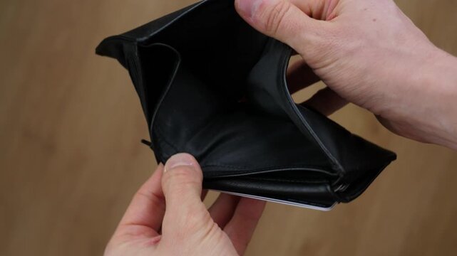 Frustrated man's hands opening an empty black leather wallet, revealing no cash, symbolizing financial crisis, bankruptcy, poverty, unemployment, and economic despair after expenses