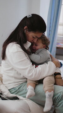 Mother holding crying toddler while showing exhaustion patience and care as child demands breastfeeding during intense parenting moment