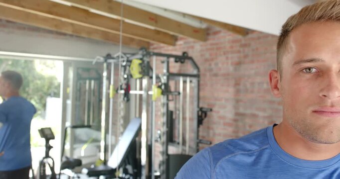 Man in blue athletic shirt reacting to mirror shifting, gradually smiling toward camera at home gym