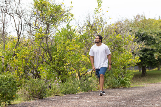African American man walking on paved park path wearing shorts, jacket tied at waist, copy space