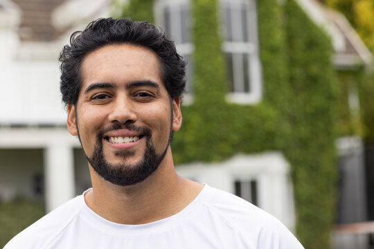 Mid adult African man smiling, standing outdoors by ivy-covered house wearing white crew-neck shirt