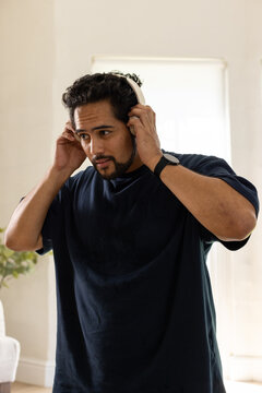 Mid adult African American man adjusting white headphones at home, wearing navy tee and smartwatch