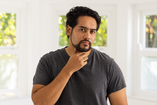 Mid-adult African American man holding chin looking in bright room in dark tee near white windows