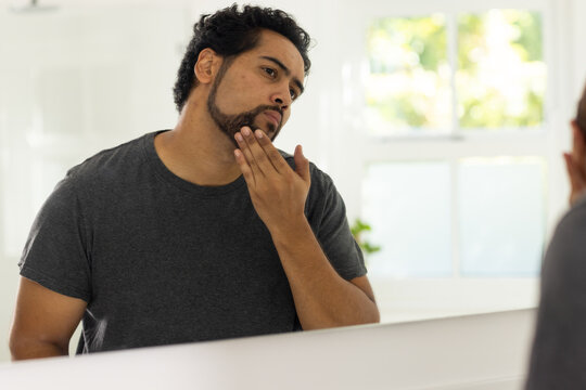 African American man touching beard and inspecting reflection at bathroom mirror