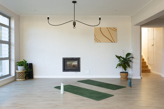 Two dark green yoga mats are resting on pale wood floor in bright room, bottles nearby