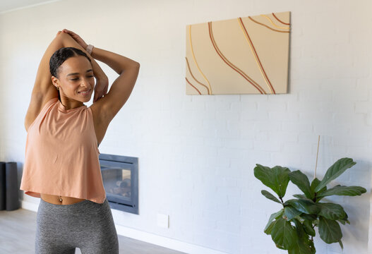 Female stretching, raising arms at home with fireplace, smartwatch, navel piercing, copy space