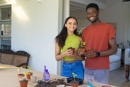 African American couple standing at home potting table holding terracotta pots and gardening tools
