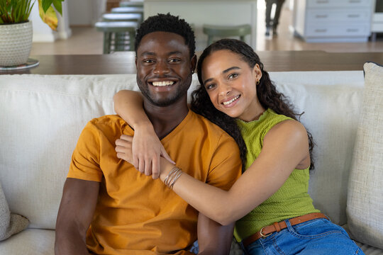 African American couple sitting closely on light fabric sofa, woman wrapping arm, bracelets visible