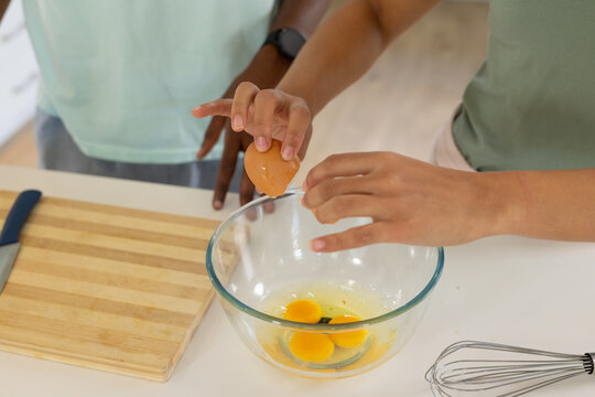 African couple cracking egg over glass mixing bowl with spoon at home kitchen countertop, knife