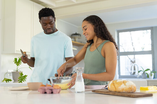 African American couple preparing batter at kitchen island woman whisking bowl as man holding knife