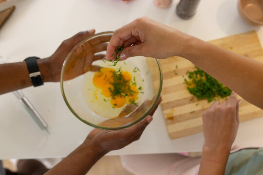 Glass mixing bowl is holding cracked egg yolks and herbs on bright countertop by cutting board