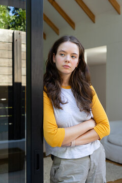 Woman leaning against dark metal sliding door frame at home, wearing mustard-sleeved raglan shirt