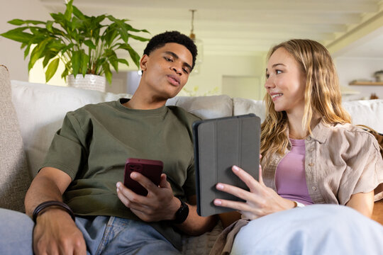 Couple with African American man and woman sitting on couch comparing smartphone and tablet folio