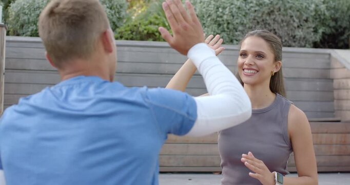 Diverse friends celebrating workout, man raising hand initiating high-five on patio with smartwatch