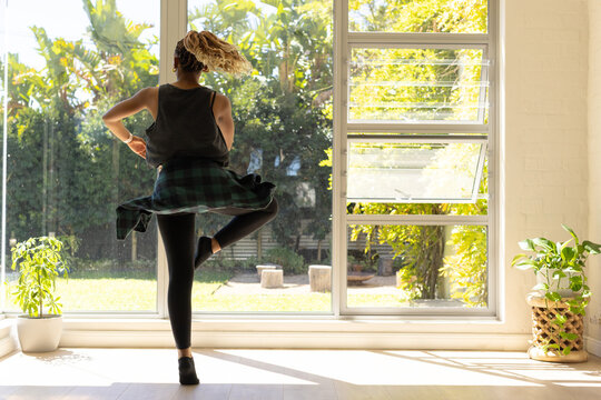 African American woman dancing, balancing near glass window with plaid shirt tied waist and plants
