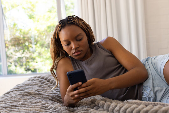 African American woman reclining on bed holding phone in gray tank, shorts on textured gray blanket