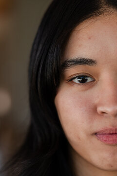 Asian female posing in softly lit interior showing tight half-face with light reflection, dark top