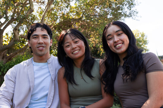Diverse friends sitting close in garden under tree with dappled sunlight, showing pendant and watch