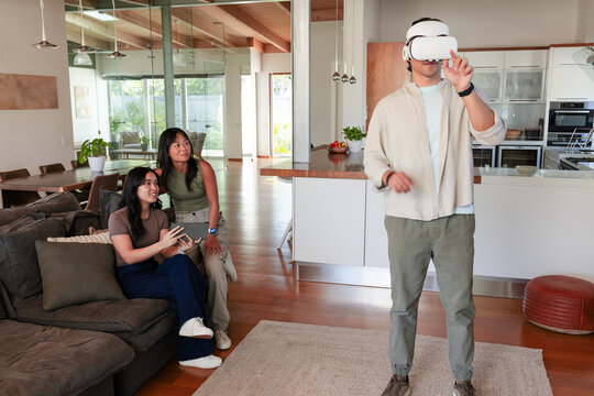 Diverse friends watching man wearing white VR headset gesturing near kitchen island, copy space