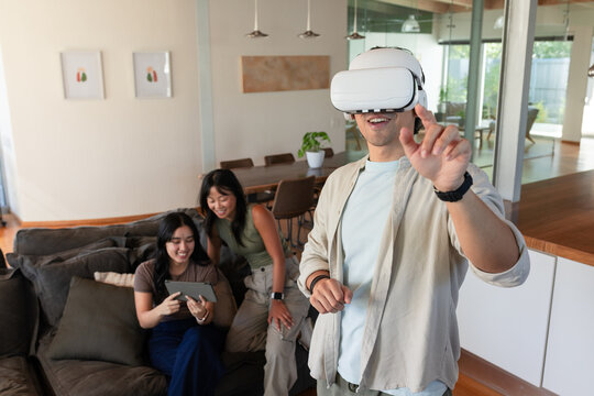 Diverse friends on sofa viewing tablet as African American man in VR headset reaching, copy space