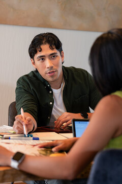 Diverse coworkers wearing green tops pointing pen at papers at meeting table next to laptop